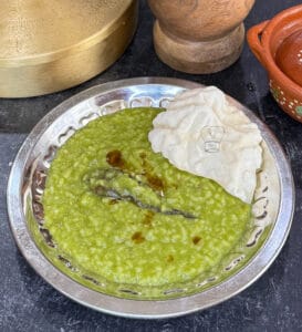 Traditional spinach and lentil khichdi served with crispy papad on a metal plate.
